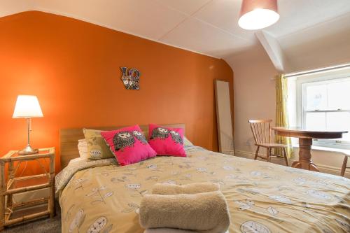 Schlafzimmer mit orangefarbenen Wänden und einem Bett mit rosa Kissen in der Unterkunft Manorbier Castle Inn Sunset Room in Tenby
