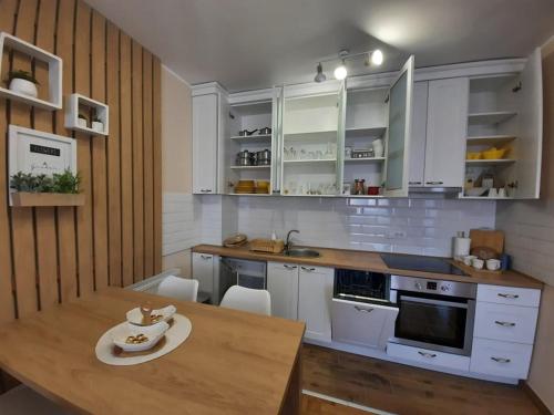 a kitchen with white cabinets and a wooden table at Apartman Ljiljana LUX Sombor in Sombor