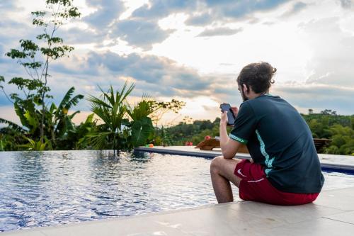 a man sitting on the edge of a pool taking a picture at Tukawa Hotel in Filandia