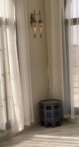 a room with white curtains and a chandelier and a table at Al Ghadeer Maison Masfout in Sharīyah