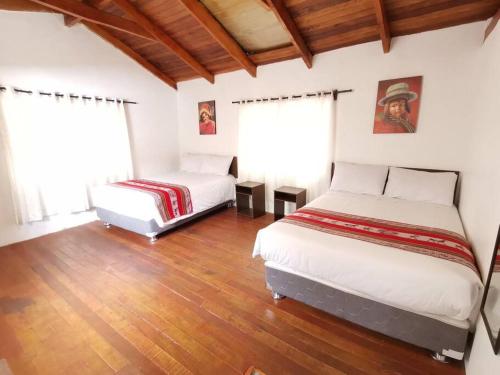 two beds in a room with wooden floors and windows at APARMENT SAMANA HOUSE OLLANTAYTAMBO in Ollantaytambo