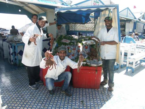 a group of men standing next to a food stand at Dar Ness in Essaouira