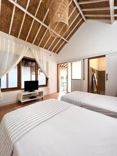 two beds in a bedroom with a tv and windows at Eden Eco Resort in Gili Trawangan