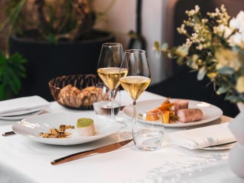 a table with two glasses of wine and plates of food at Balthazar Hotel & Spa Rennes - MGallery Collection in Rennes