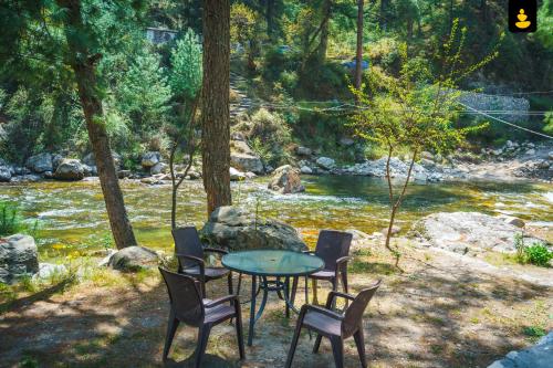 a table and chairs sitting next to a river at LivingStone Backwater Resort Tirthan Valley in Banjār