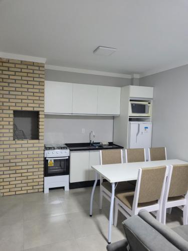 ガロパバにあるNOVO LAR GAROPABA 2の白いキャビネット、テーブルと椅子付きのキッチンが備わります。