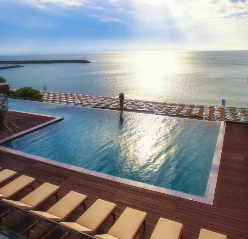 a swimming pool with chairs and the ocean in the background at GRIFID Encanto Beach Hotel - MediSPA, Ultra All Inclusive & Private Beach in Golden Sands