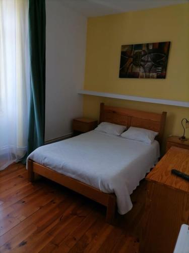 a bedroom with a bed with white sheets and wooden floors at PENSÃO AVENIDA in Penacova