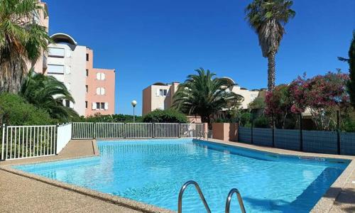 une grande piscine bleue avec des palmiers et des bâtiments dans l'établissement Appartement GRUISSAN Plage du Grazel, à Gruissan