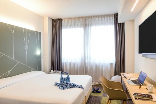 アグラーテ・ブリアンツァにあるMercure Milano Agrate Brianzaのベッド、デスク、ノートパソコンが備わるホテルルームです。