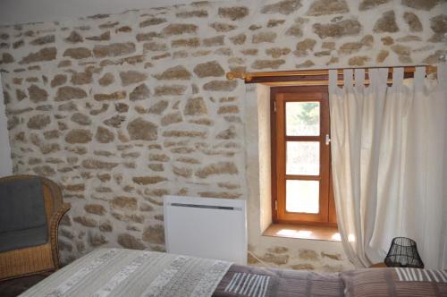 a bedroom with a stone wall and a window at LA MAGNANERIE in Grillon