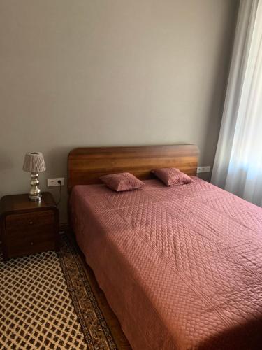 um quarto com uma cama com lençóis cor-de-rosa e um candeeiro em Cathedral Apartments em Kaunas