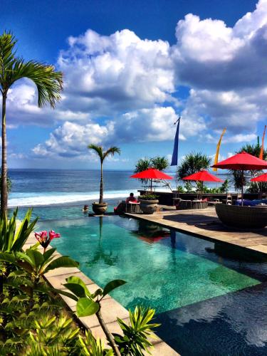 a swimming pool with red umbrellas and the ocean at The Palms Ceningan Hotel in Nusa Lembongan