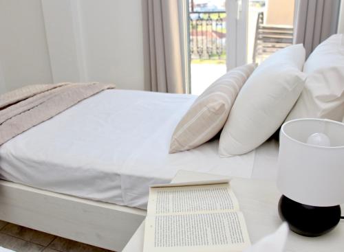 un letto con cuscini bianchi e un libro su un tavolo di Lightful Attic at Regina Apartments ad Alikanás