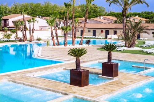 a swimming pool with palm trees and a resort at Maison avec piscine chauffée de Pâques à la toussaint accès animation & parc aquatique de juin à fin septembre in Portiragnes