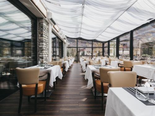 a restaurant with white tables and chairs and windows at Hotel Victoria by VAYA in Kaprun