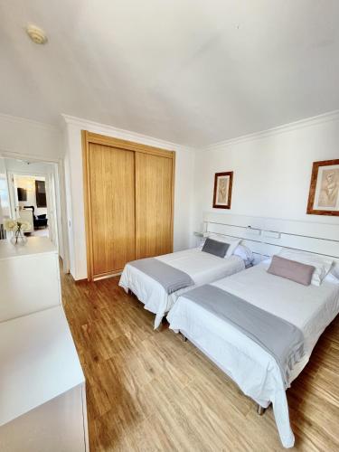 2 Betten in einem Zimmer mit weißen Wänden und Holzböden in der Unterkunft Casahost - Casa Elu Lanzarote in Puerto del Carmen