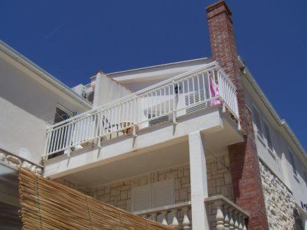 una casa blanca con un balcón con una mujer. en Apartments Mediteraneo, en Klek