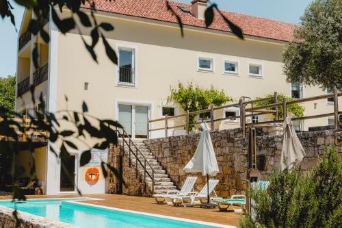 a swimming pool with two umbrellas and chairs next to a building at Retiro do Bosque Country House in Minde