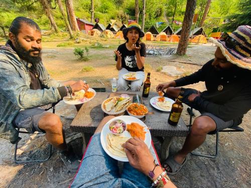 un grupo de personas sentadas alrededor de una mesa de picnic comiendo comida en Himtrek Riverside Camps, Kasol, en Kasol