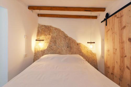 Cama blanca en habitación con pared de piedra en Blue Vorna, en Ano Syros