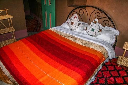 a bed with a red and orange blanket and pillows at Kasbah Maison D’hôte Lalla Zahra in Aït Baha