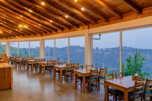 a dining room with tables and chairs and windows at Shivoham Himalayan Resort in Almora
