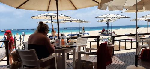 a woman sitting at a table in front of the beach at Atlantic Sal Hostel in Santa Maria