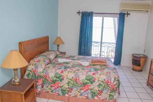 sypialnia z łóżkiem z kwiatową narzutą i oknem w obiekcie The Buccaneer w mieście Montego Bay