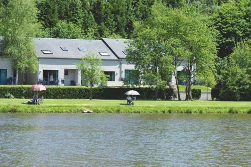 a house next to a lake with people sitting under umbrellas at Bord de lac - 4/6pers SAUNA - terrasse 20m2 in Vielsalm