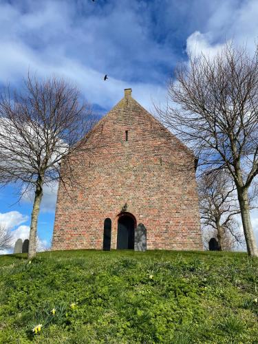a brick building on a hill with two trees at Ollediek in Houwerzijl