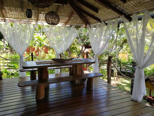 um deque de madeira com uma mesa e cortinas brancas em Bangalô alto do Mucugê em Arraial d'Ajuda
