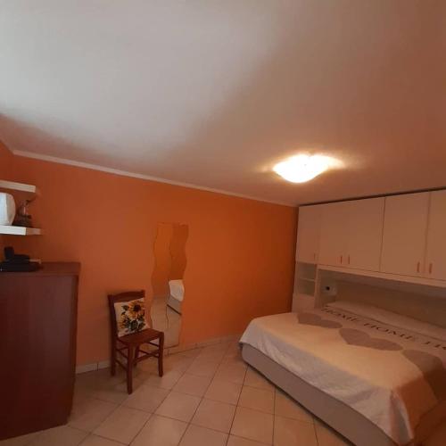 1 dormitorio con paredes de color naranja, 1 cama y 1 silla en Le tue vacanze a Varzo, appartamento il girasole. en Varzo
