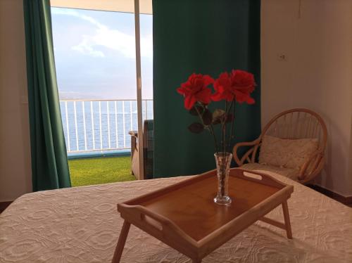 a vase with red flowers on a table with a window at Beautiful beach in Santa Cruz de Tenerife