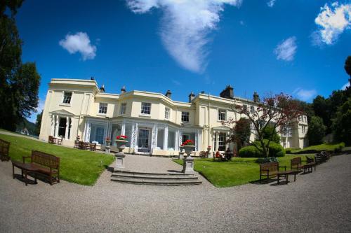 a large white house with benches in front of it at Storrs Hall Hotel on the shore of Lake Windermere in Bowness-on-Windermere