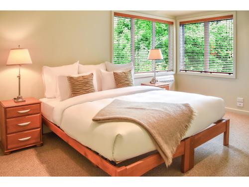 a large white bed in a bedroom with two windows at River Birches in Turangi