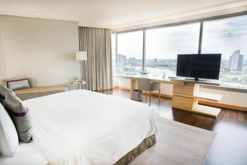 a hotel room with a bed and a desk with a television at Avani Plus Riverside Bangkok Hotel in Bangkok