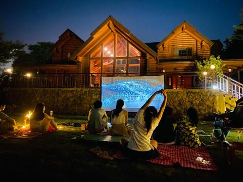 Eine Gruppe von Menschen, die auf dem Rasen sitzen und einen Film sehen in der Unterkunft Wooden 北美莊園 in Miaoli