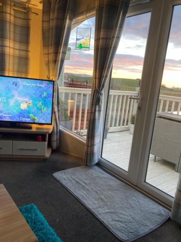 a living room with a television and a balcony at Carnoustie 24 - Turnberry Holiday Park - short walk to beach in Girvan