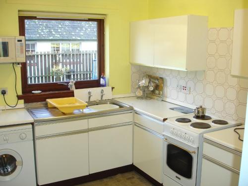 cocina con armarios blancos, fregadero y ventana en Lavender Cottage with Parking and Beautiful Views en Carsphairn