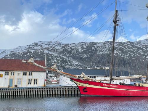a red boat sitting in the water next to a building at 1. etg i Dampskipsbrygga, Lødingen havn in Lødingen