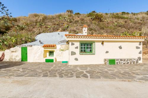 ein kleines weißes Haus mit grünen Türen auf einem Hügel in der Unterkunft La Cueva de Tito-Casa Cueva en plena naturaleza in Santa Brígida