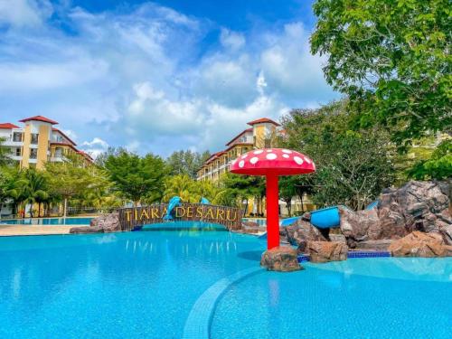 een zwembad in een attractiepark met een rode parasol bij THRE @ Tiara desaru [Private Apartment with Beach] in Bandar Penawar