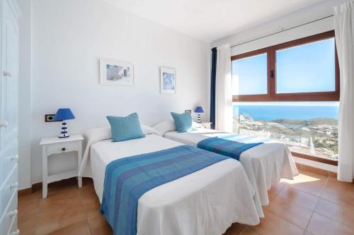 two beds in a white room with a large window at Villa Amanecer by Villa Plus in Cumbre del Sol
