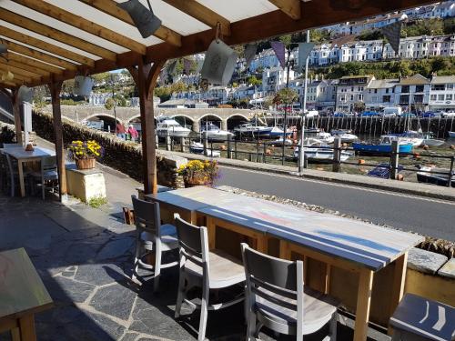 uma mesa de madeira e cadeiras sob um telhado de madeira com uma marina em The Harbour Moon em Looe