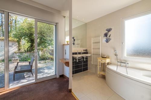 a bathroom with a tub and a sink and a window at Domaine de l'Echassier, The Originals Relais in Châteaubernard