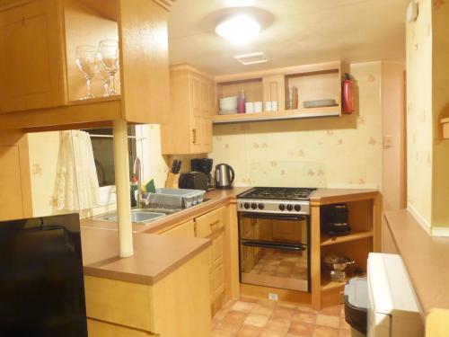 a kitchen with wooden cabinets and a stove top oven at Beachside, Family-friendly, WiFi, 6 berth Caravan 12 in Ingoldmells