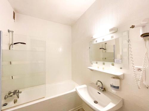 La salle de bains blanche est pourvue d'un lavabo et d'une baignoire. dans l'établissement Hotel les Alignements, à Carnac