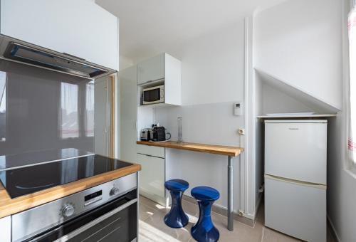 une cuisine avec des placards blancs et des tabourets bleus dans l'établissement Callisto, à Luc-sur-Mer