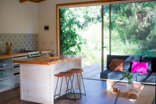 cocina y sala de estar con una gran ventana de cristal en Cabaña a pasos del río rodeada de un hermoso entorno nativo natural, en Villarrica